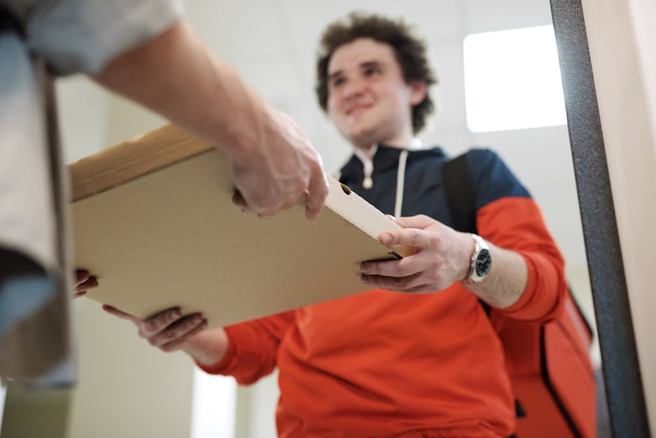 Smiling deliveryman handing over pizza box indoors, offering service.