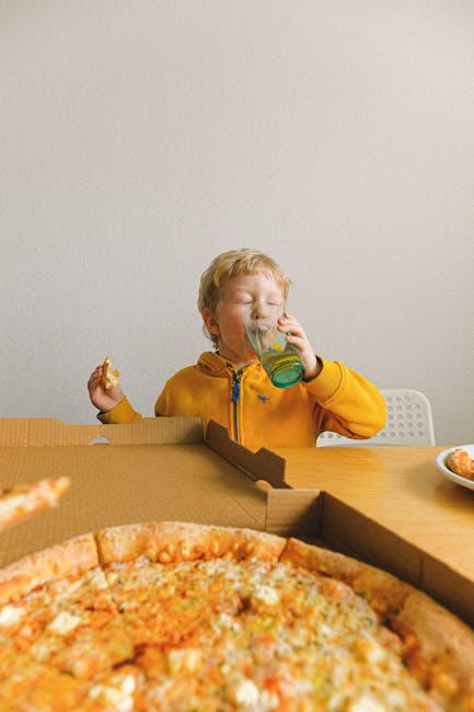 Boy in yellow jacket savoring pizza and a drink at home, creating a cozy dining scene.